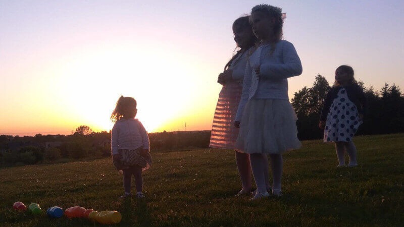 Silhouetted children on a grassy hill at sunset, with colorful toys scattered in the foreground.