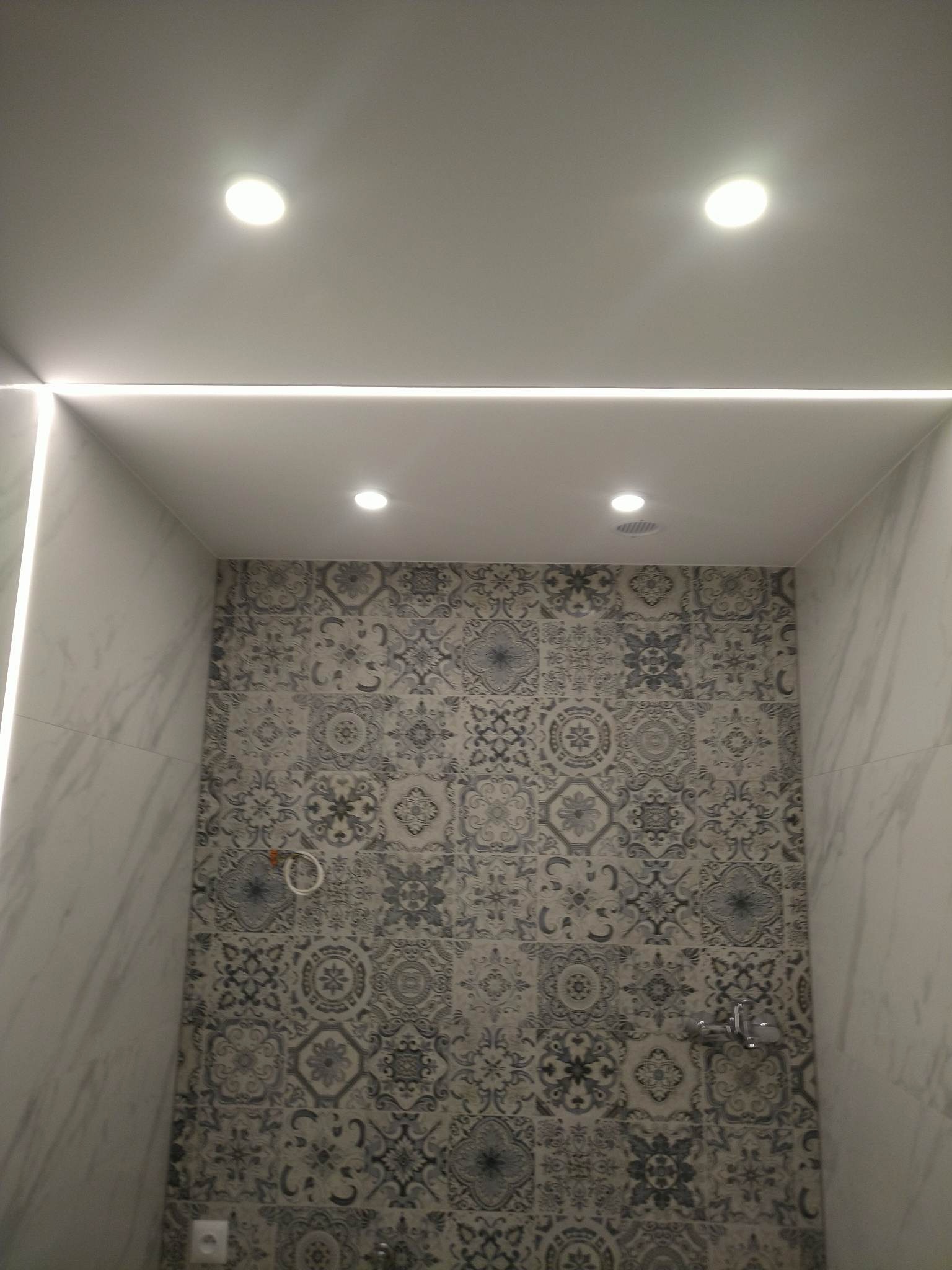 Wykończona łazienka z dekoracyjnymi płytkami ściennymi w odcieniach szarości, oświetleniem sufitowym punktowym i liniowym LED.