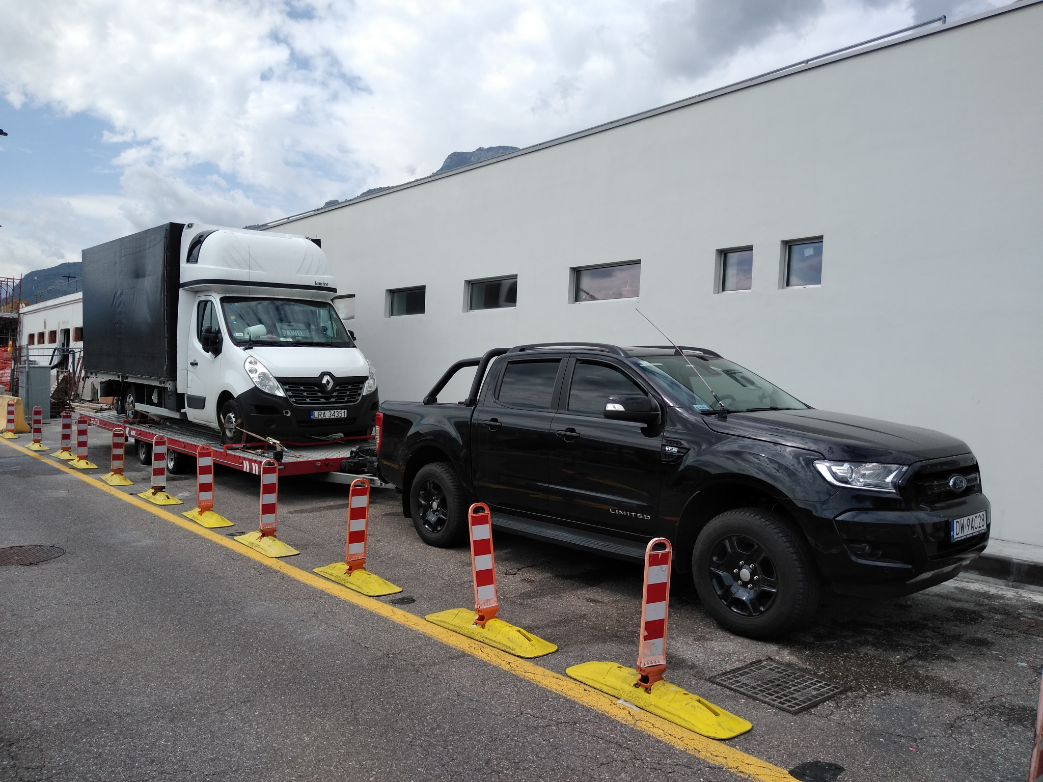 Czarny Ford Ranger Limited stoi obok lawety z białym Renault Master z plandeką na tle białego budynku z małymi oknami.