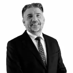 Portret uśmiechniętego mężczyzny w garniturze i krawacie z wzorem paisley, zdjęcie czarno-białe.