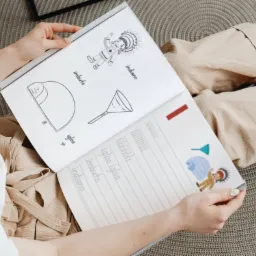 Osoba trzyma otwarty zeszyt z rysunkami i słowami po włosku: igloo, imbuto, indiano, prezentujący naukę słownictwa.