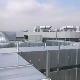 Widok z góry na rozbudowany system kanałów wentylacyjnych i centrali na dachu budynku komercyjnego, z widocznym logo CIAT na jednej z central, w tle błękitne niebo z chmurami.