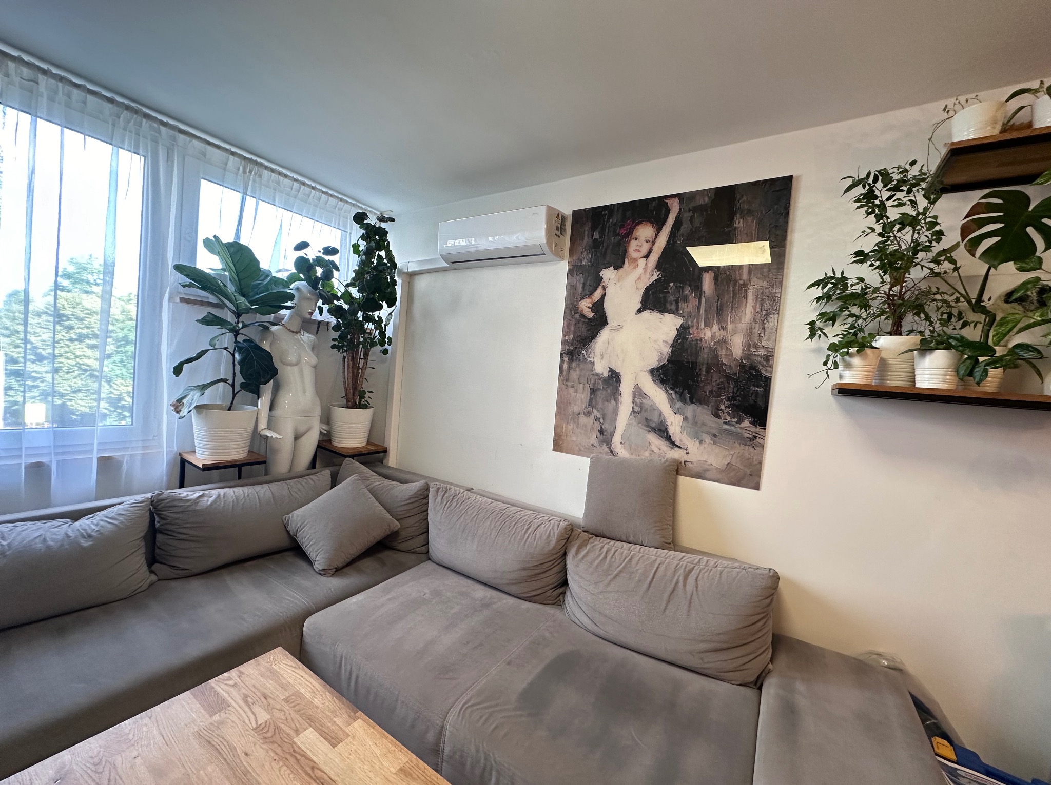 Wnętrze salonu w Krakowie z zamontowaną klimatyzacją typu split nad obrazem baletnicy, widok na szarą sofę narożną, rośliny doniczkowe i manekin.