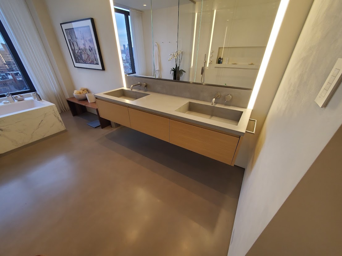 Nowoczesna łazienka z podwójną umywalką z szarego betonu i drewnianymi szafkami wiszącymi podświetlonymi ledami, na tle okna z widokiem na miasto.