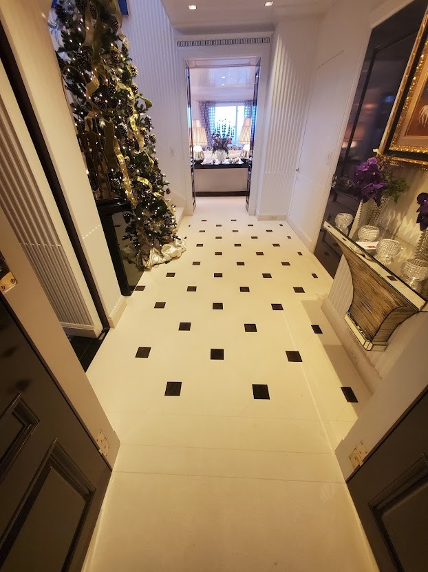 Hallway with white floor and black square tiles, Christmas tree on the left, console table with flowers on the right, and a view into another room in the background.