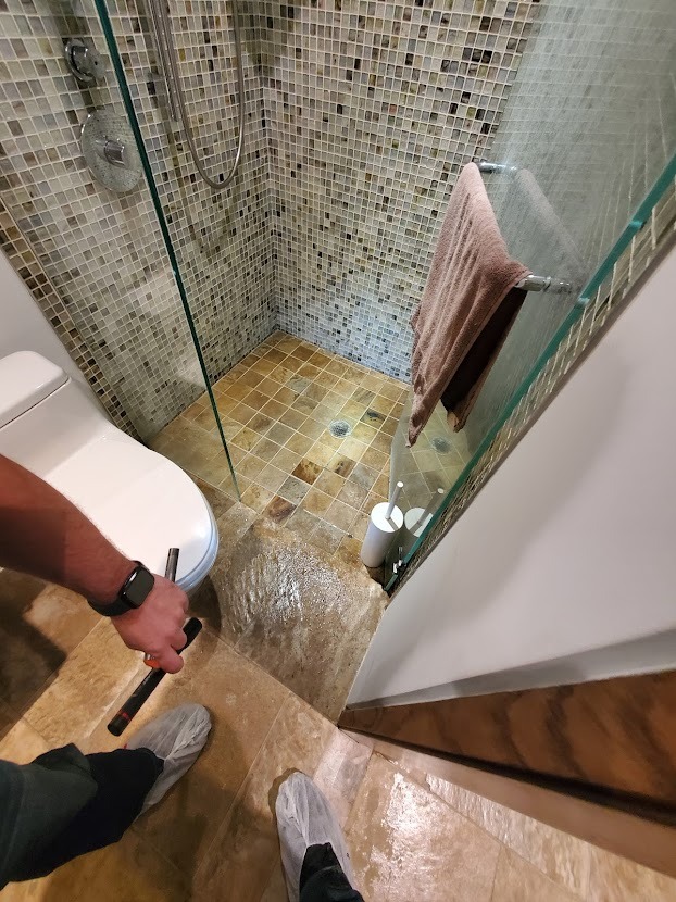 Nowoczesna kabina prysznicowa z mozaikową ścianą, widok z góry na osobę w ochraniaczach na buty podczas sprawdzania szczelności po montażu.