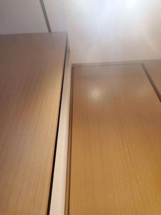 Fragment szafy z jasnego drewna, wykonanej na wymiar w Rzeszowie, z widocznymi detalami wykończenia i białymi elementami konstrukcyjnymi.