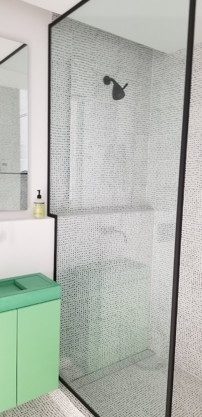 Nowoczesna kabina prysznicowa z czarnymi ramami i deszczownicą, białe ściany z drobnym wzorem, obok umywalka z szafką w odcieniu zieleni.