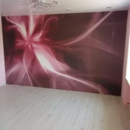 Pokój z fototapetą o abstrakcyjnym wzorze w odcieniach różu i bieli, jasne panele podłogowe, nowoczesna lampa sufitowa.