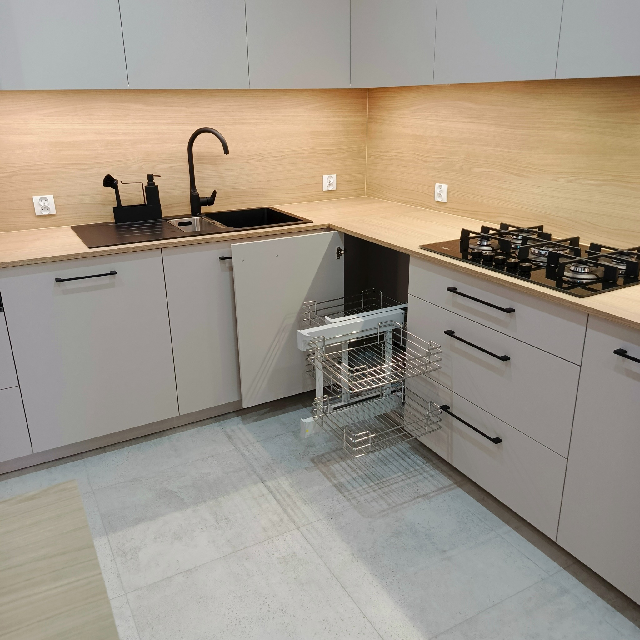Jasna kuchnia z drewnianym blatem, czarną armaturą i wysuwanym koszem cargo w szafce narożnej. Minimalistyczny design z subtelnym oświetleniem.