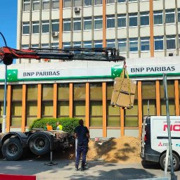 Nosek- Serwis Chłodniczy - Rozładunek klimatyzatorów GREE z samochodu ciężarowego z dźwigiem Palfinger przed budynkiem BNP Paribas, widoczny samochód serwisowy firmy Nosek z logo Midea, Daikin i Mitsubishi Electric.