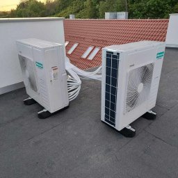 Nosek- Serwis Chłodniczy - Dwa białe agregaty klimatyzacyjne marki Hisense, zamontowane na płaskim dachu budynku z widocznymi przewodami i fragmentem dachu skośnego z oknami.