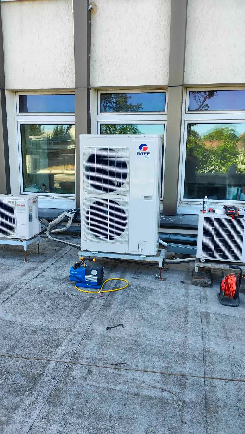 Instalacja zewnętrznych jednostek klimatyzacji na dachu budynku, widoczna pompa próżniowa i narzędzia serwisowe, jednostki marek Gree i Fujitsu.