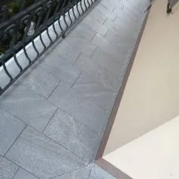 Szare płytki ułożone na balkonie z ozdobną, metalową barierką, widok z góry.