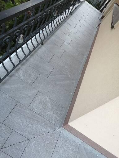 Szare płytki ułożone na balkonie z ozdobną, metalową barierką, widok z góry.