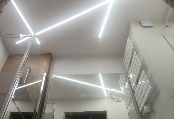 Nowoczesna łazienka w Skierniewicach z podświetlanym sufitem i szklaną kabiną prysznicową, widok z dołu na geometryczne linie świetlne.