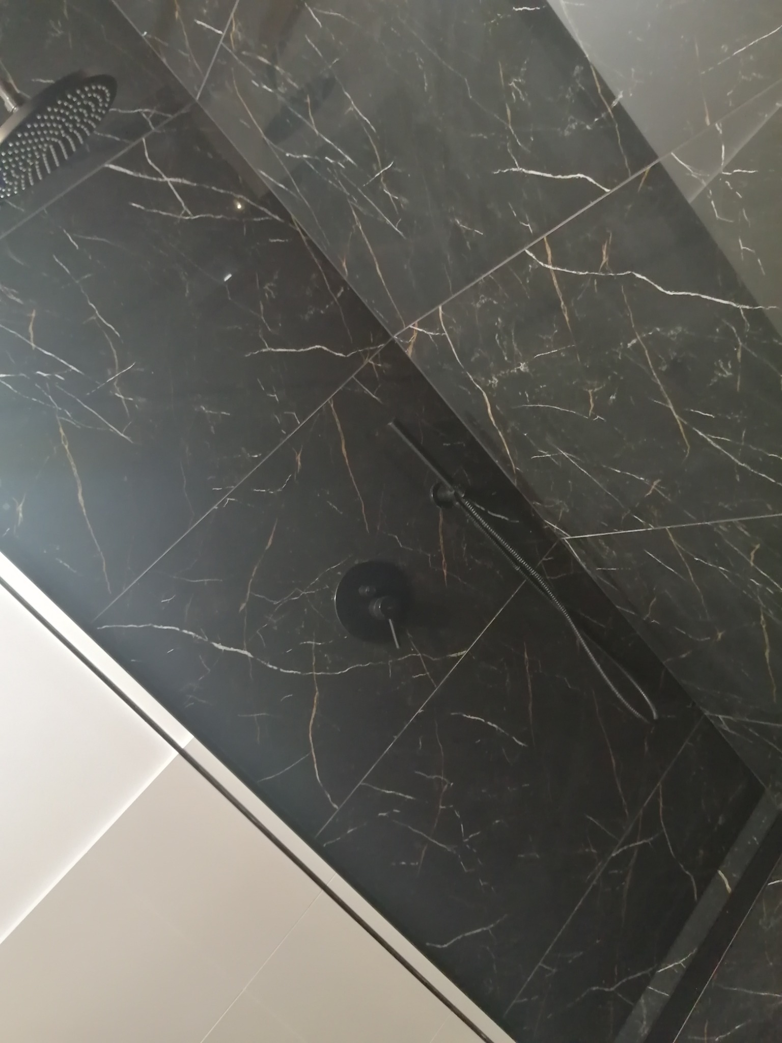 Kabina prysznicowa z czarnymi płytkami imitującymi marmur z białymi żyłami, czarna deszczownica i bateria, widok z dołu.