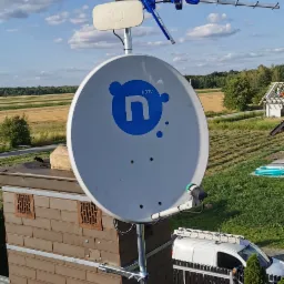 Antena satelitarna i antena DVB-T zamontowane na kominie, widoczny krajobraz wiejski w tle.