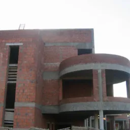 Wznoszenie dwukondygnacyjnego budynku z czerwonej cegły z balkonem o zaokrąglonym kształcie, widoczne surowe ściany i betonowe elementy konstrukcyjne, drabina oparta o ścianę.