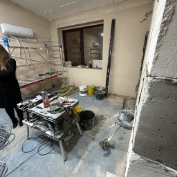 Kamar KAMIL ŚWICA - Wnętrze w trakcie prac budowlanych: widoczny stół roboczy z narzędziami, drabina, poziomica, szpachla elektryczna przy ścianie z betonu komórkowego, worki i pojemniki z materiałami budowlanymi...