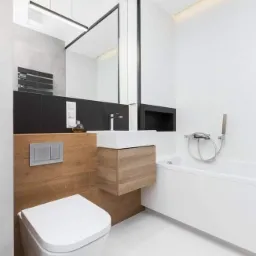 Nowoczesna łazienka w bieli z drewnianymi akcentami, podwieszana toaleta, umywalka z szafką i minimalistyczna armatura.