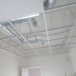 Montaż sufitu podwieszanego kasetonowego z widocznymi instalacjami wentylacyjnymi i kablami w jasnym pomieszczeniu.