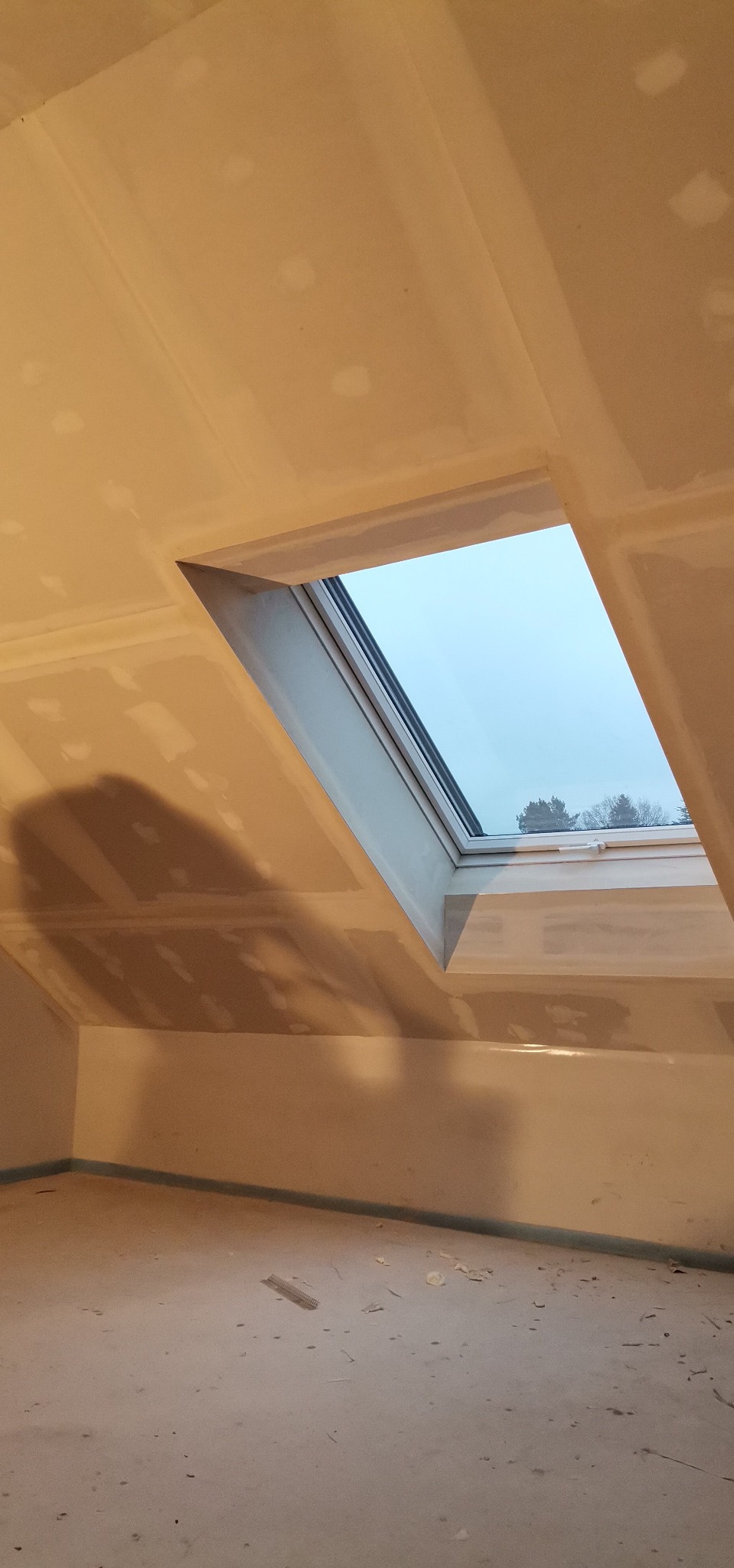 Poddasze z oknem dachowym w trakcie wykańczania płytami kartonowo-gipsowymi, widoczne łączenia wymagające szpachlowania i szlifowania.
