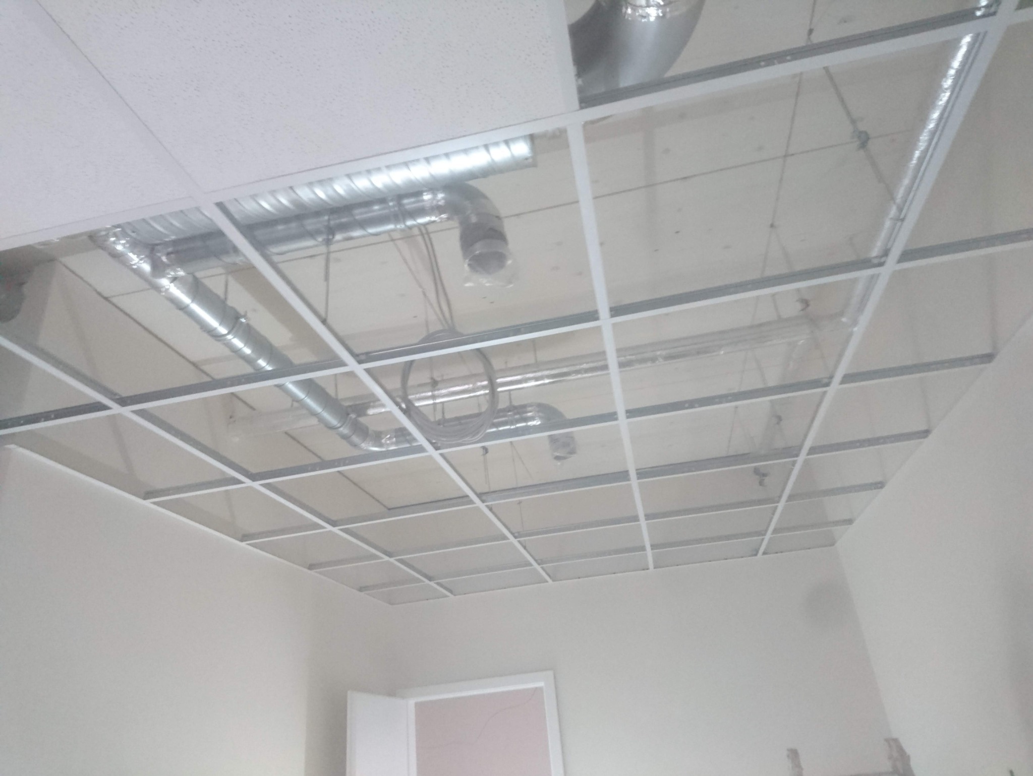 Montaż sufitu podwieszanego kasetonowego z widocznymi instalacjami wentylacyjnymi i kablami w jasnym pomieszczeniu.