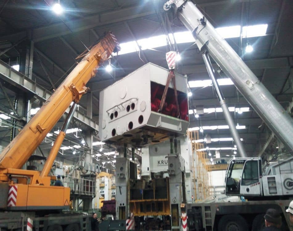 Usługi dźwigowe w Bielsko-Białej: Dwa dźwigi, jeden pomarańczowy i jeden srebrny, unoszą duży, biały element maszyny z widocznym napisem 'KRU'.