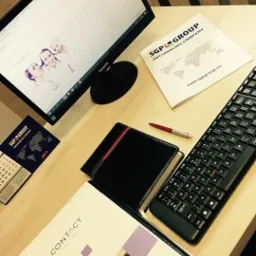 Biurko z monitorem wyświetlającym stronę internetową, folderem 'Contact Solutions', kalendarzem firmowym SGP Group, czarnym portfelem z czerwonym paskiem i klawiaturą.