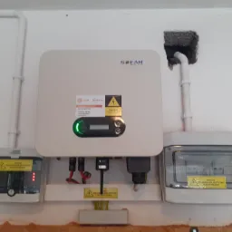 Zamontowany inwerter SOFAR z podłączonymi zabezpieczeniami elektrycznymi na białej ścianie z widocznymi przewodami i rurami instalacyjnymi.