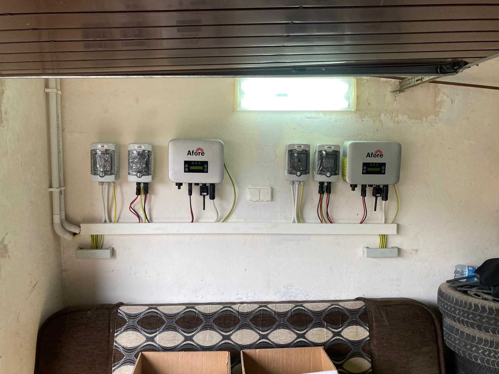 Instalacja fotowoltaiczna w garażu: Inwertery marki Afore zamontowane na ścianie nad starą kanapą i oponami samochodowymi, częściowo jeszcze w folii ochronnej.