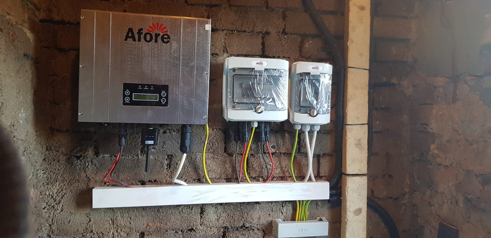 Zamontowany srebrny falownik Afore z podłączonymi przewodami na ceglanej ścianie, obok białe skrzynki zabezpieczeń w folii ochronnej.