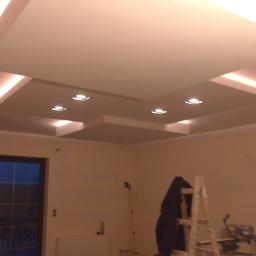 Arek Bancer - Wykończony sufit podwieszany z oświetleniem punktowym, widoczna drabina i narzędzia malarskie w tle, sugerujące trwające prace wykończeniowe.