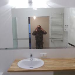 Arek Bancer - Nowoczesna łazienka z białą umywalką na drewnianym blacie, widoczny grzejnik drabinkowy i odbicie fotografa w lustrze.