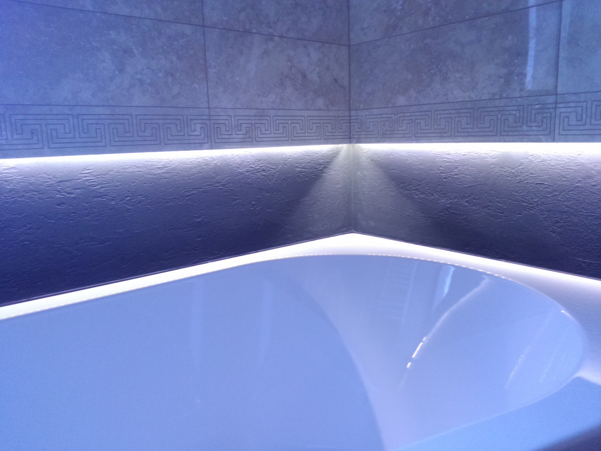 Nowoczesna łazienka z podświetlaną wanną, ściany wykończone szarymi płytkami z geometrycznym wzorem i ukrytym oświetleniem LED.