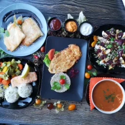 Zestaw r&oacute;żnorodnych dań na ciemnych talerzach: naleśniki z sosem czekoladowym, smażony filet z kaszą i warzywami, sałatka z burakiem, ryba z ryżem i warzywami oraz zupa pomidorowa, udekorowane...