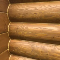 Fragment ściany zewnętrznej domu z bali, pokazujący łączenie bali w rogu, widoczne słoje drewna i impregnacja w odcieniach brązu.