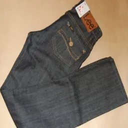 Ciemne jeansy marki Lee z brązową naszywką z logo na tylnej kieszeni, leżące na beżowym tle.