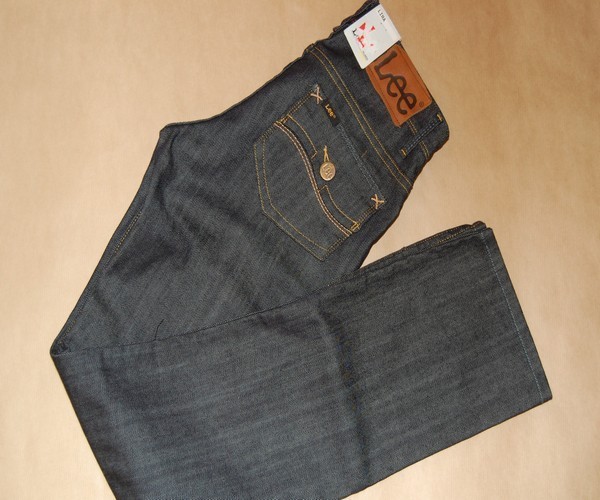 Ciemne jeansy marki Lee z brązową naszywką z logo na tylnej kieszeni, leżące na beżowym tle.