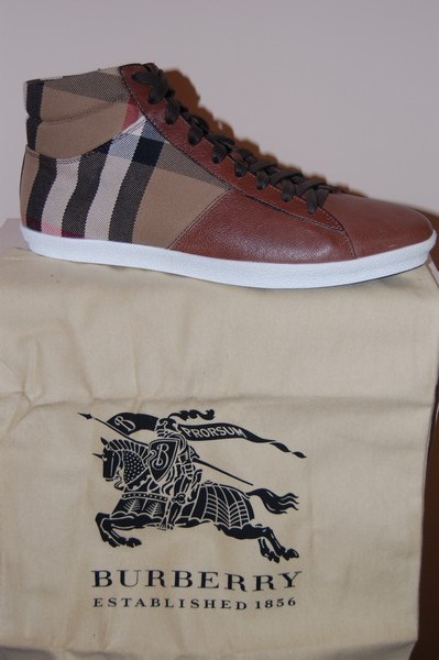 Brązowy skórzany but sportowy Burberry z charakterystycznym kraciastym wzorem na cholewce, ustawiony na beżowym worku z logo marki.