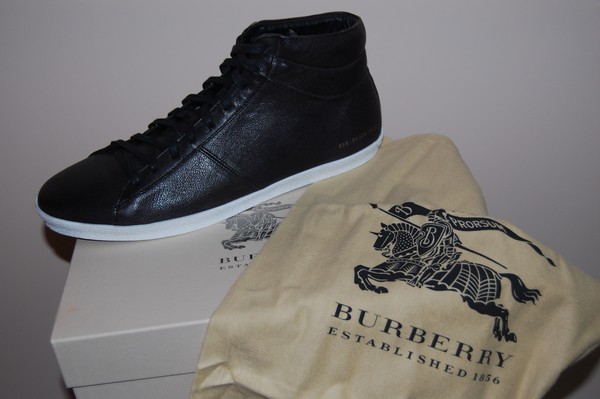 Czarny skórzany but sportowy Burberry na białej podeszwie, leżący na pudełku obok beżowego worka z logo marki.