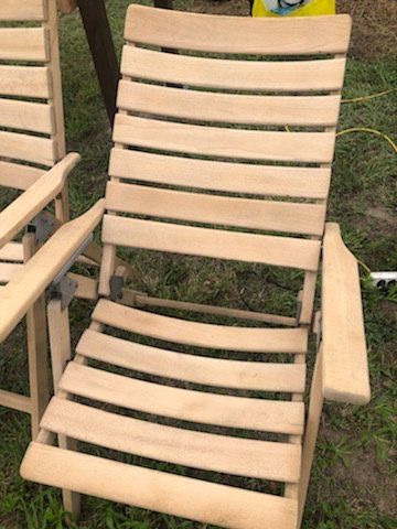 Drewniane krzesło ogrodowe z listew po renowacji, widoczne metalowe zawiasy, jasne drewno, tło z trawy.