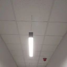 Sufit podwieszany z oświetleniem rastrowym w korytarzu biurowym w Toruniu, widoczny czujnik dymu.