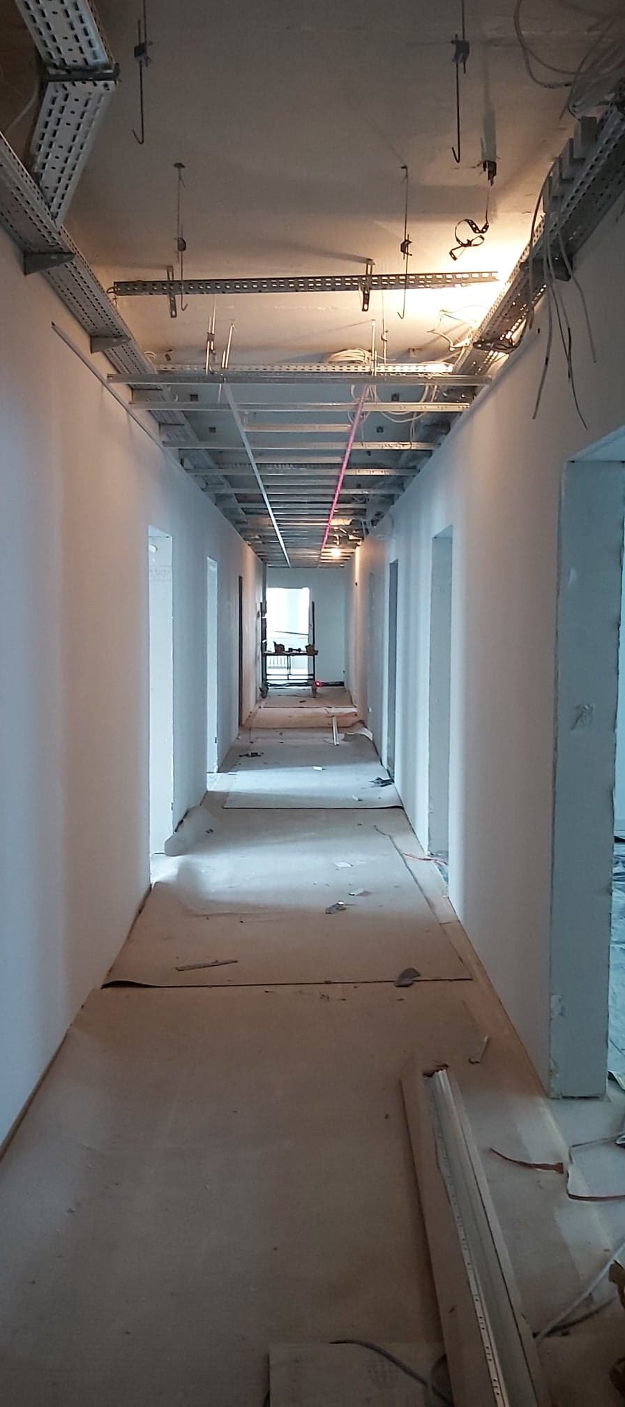 Korytarz biurowy w trakcie malowania ścian, widoczne instalacje pod sufitem i laserowy niwelator