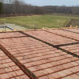 Wypełniony pustakami ceramicznymi strop Teriva, widok z góry na konstrukcję zbrojeniową na tle krajobrazu z drzewami i polem.