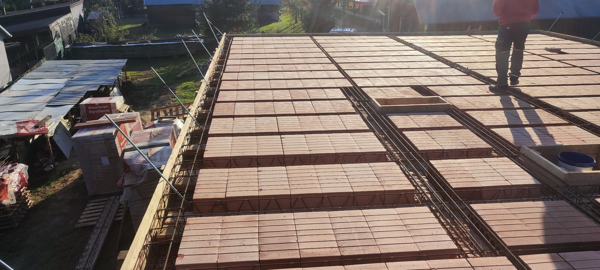 Układanie stropu Teriva z pustaków ceramicznych i zbrojenia stalowego, widoczne materiały budowlane Porotherm i pracownik w oddali.