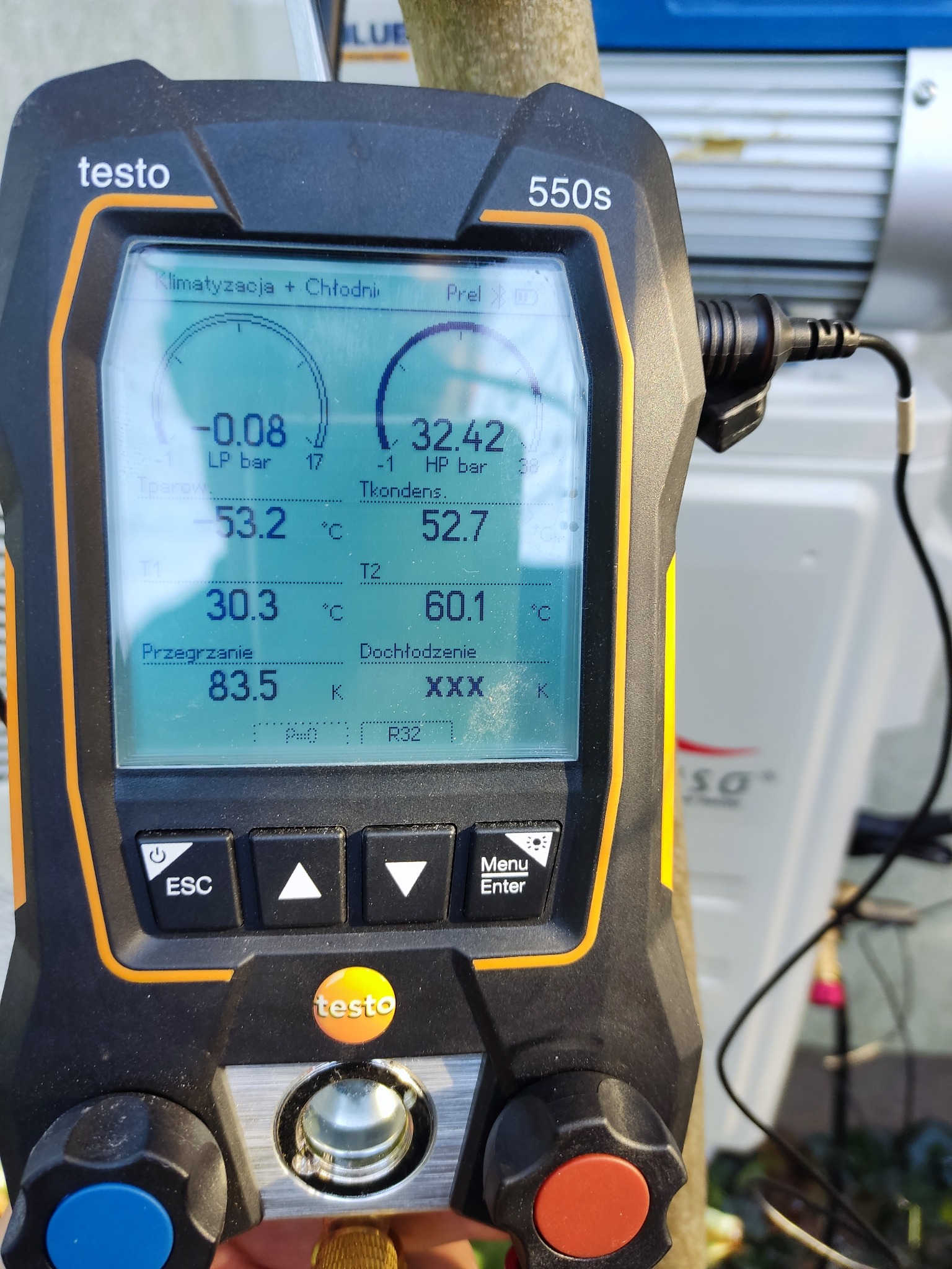 Miernik elektroniczny Testo 550s wyświetlający parametry pracy układu chłodniczego, z widocznymi wartościami ciśnienia, temperatury i przegrzania, na tle jednostki zewnętrznej klimatyzatora.