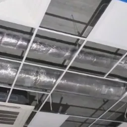 Sufit podwieszany z widoczną instalacją wentylacyjną i klimatyzacją, częściowo zamontowane białe panele, niebieska taśma malarska na obrzeżach.