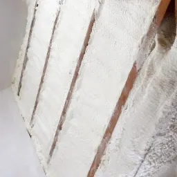 Poddasze ocieplone białą pianką poliuretanową między drewnianymi krokwiami, widoczne detale struktury pianki i folii ochronnej. Na dole logo firmy Burzy-Bud.